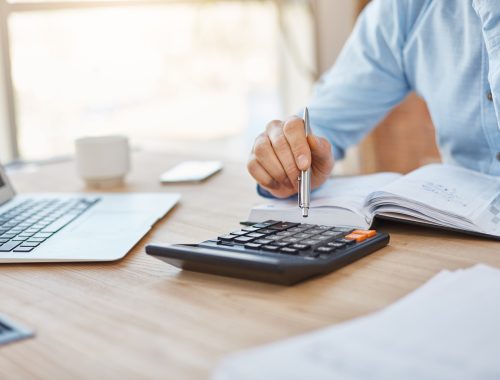 Close up detail of professional serious accountant sitting in light office, checking company finance profits on calculator, writing down results in notebook. Business concept